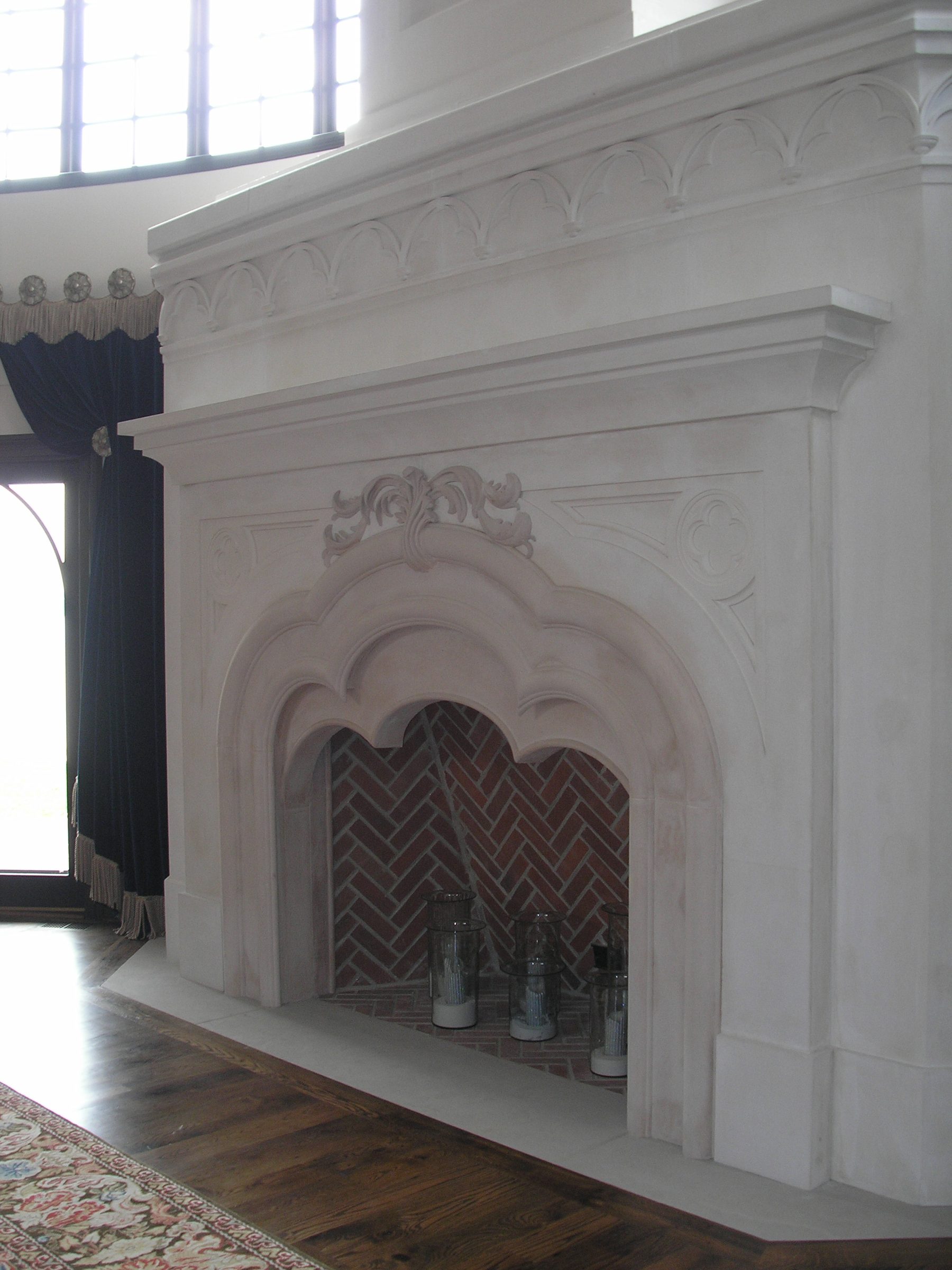 A cast-plaster fireplace with an ogee-arched opening, a carved acanthus crest and a herringbone-brick firebox.