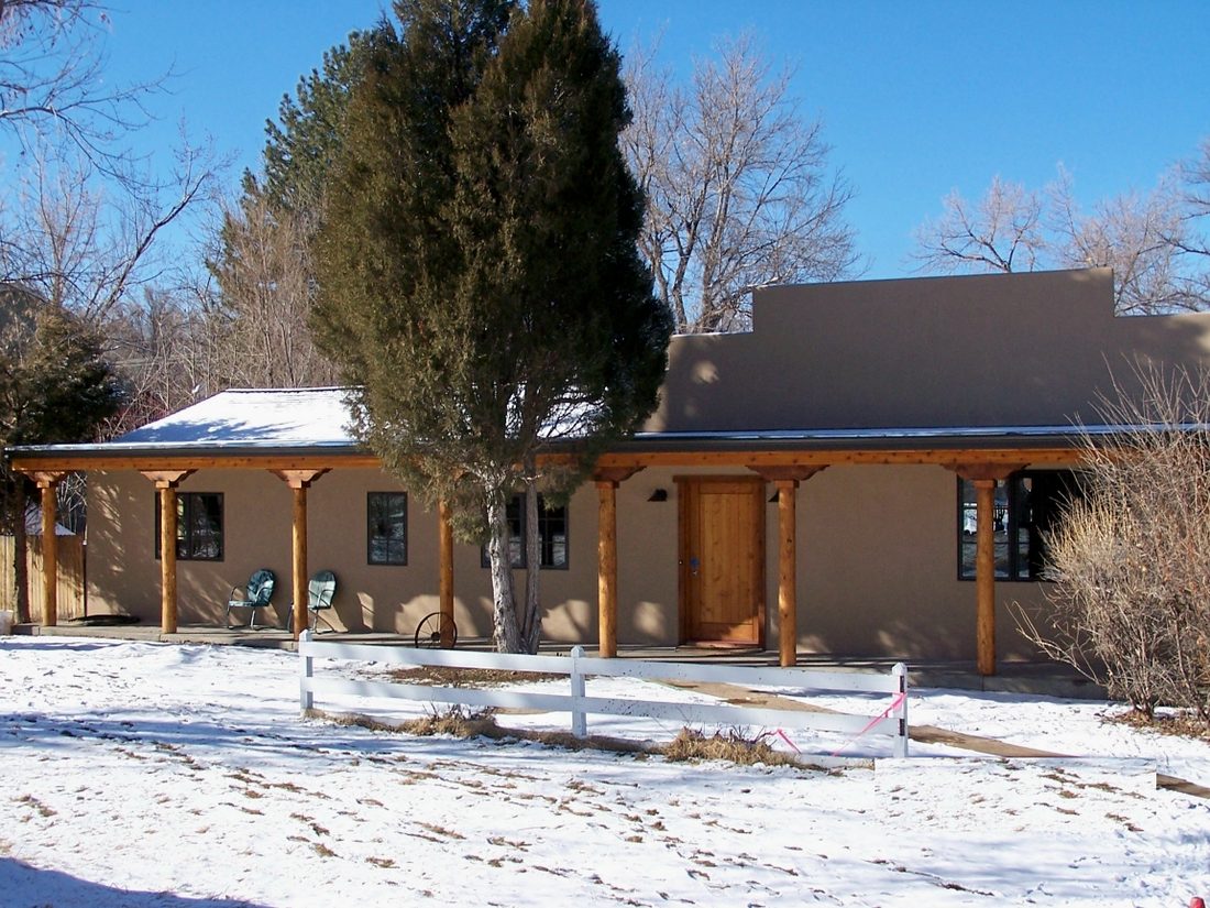 A renovated Santa Fe-style rancher with stucco walls and a timber-post porch under Colorado snow.