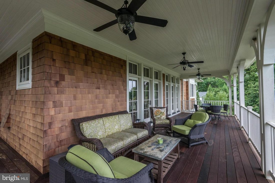 The deep wraparound porch in cedar shake, with ceiling fans, wicker seating and a painted bead-board ceiling.
