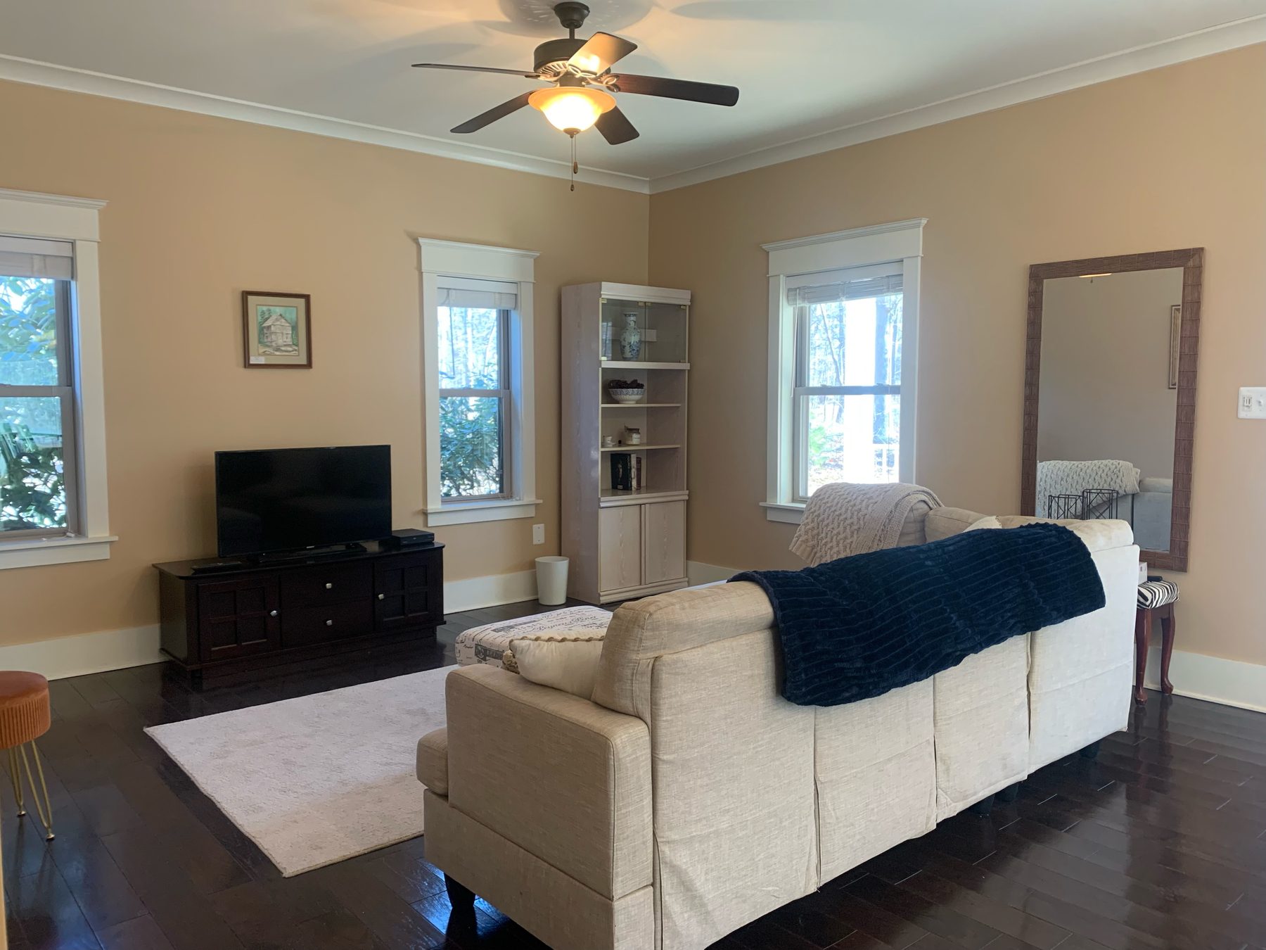 The living room — warm walls, wide hardwood floors and generous window openings framing the surrounding woods.